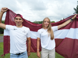 Meitene un zēns aiz muguras tur Latvijas karogu