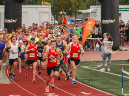 Daudz cilvēku sporta tērpos skrien pa oranžu skrejceliņu