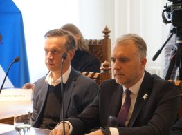 Divi vīrieši pie galda ar mikrofoniem sanāksmē