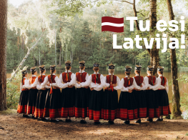 Meitenes tautastērpos zaļā brīvdabā ar baltu teksta grafiku