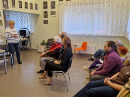 Cilvēku grupa gaišā telpā sēž klausās nodarbību