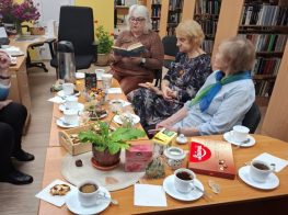 Grāmatu klubiņa tikšanās telpā ar dzeltenām sienām un grāmatu skapjiem