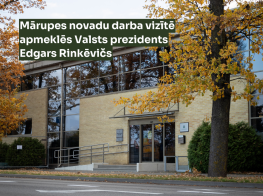 Ēkas bilde rudenī ar tumši zaļu tekstu virsū