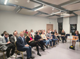 Darba grupas dalībnieki sēž krēslos gaišā telpā