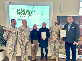 Seši cilvēki stāv kājās, fonā ekrāns