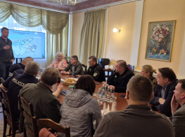 telpa ar galdu, ap kuru sēž cilvēki sapulcē